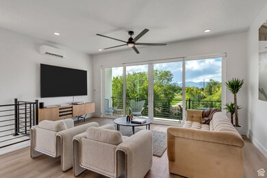 Living area with a ceiling fan, recessed lighting, light wood-style floors, and an AC wall unit