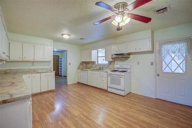 Kitchen featuring white appliances, under cabinet range hood, light countertops, light wood-style flooring, and a textured ceiling