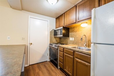 Kitchen with freestanding refrigerator, decorative backsplash, black range with gas stovetop, dark wood-style flooring, and stainless steel microwave