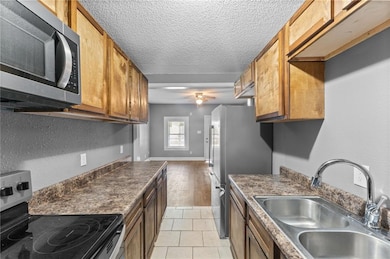 Kitchen with stainless steel appliances, a textured ceiling, light tile patterned floors, dark countertops, and a ceiling fan
