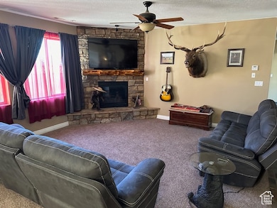 Living room with a stone fireplace, a textured ceiling, carpet flooring, and ceiling fan