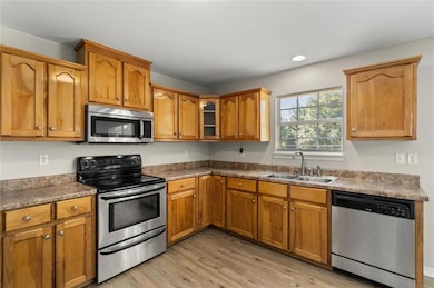 Kitchen featuring stainless steel appliances, light wood-style floors, brown cabinets, glass insert cabinets, and recessed lighting