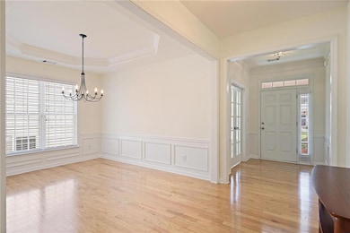 Foyer entrance with a chandelier, ornamental molding, light wood-style floors, wainscoting, and a decorative wall