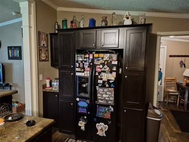 Bar with ornamental molding, a textured ceiling, black fridge with ice dispenser, and dark wood-style flooring
