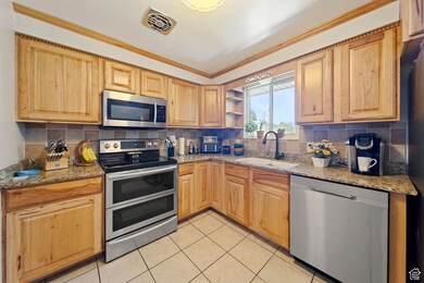 Kitchen with light stone countertops, stainless steel appliances, backsplash, crown molding, and open shelves
