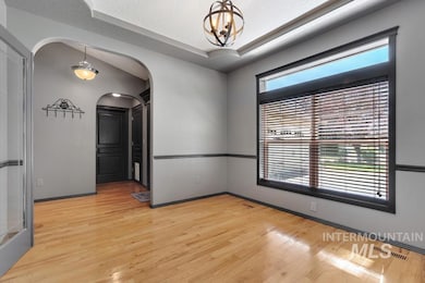 Empty room featuring light wood-style flooring, a raised ceiling, arched walkways, and a chandelier