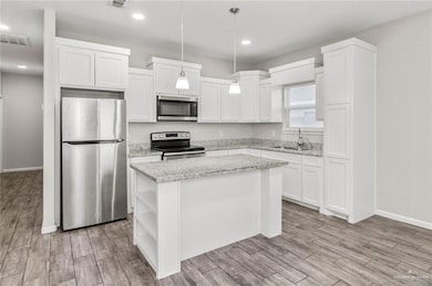 Kitchen featuring open shelves, a center island, a sink, visible vents, and appliances with stainless steel finishes