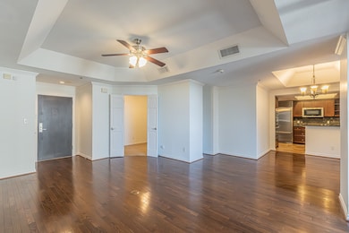 Unfurnished living room with a tray ceiling, crown molding, dark wood-style floors, a ceiling fan, and a chandelier