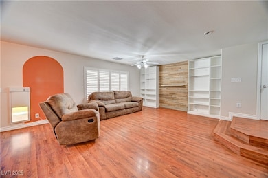 Living area with a textured ceiling, a ceiling fan, light wood-style floors, and built in shelves