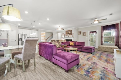 Living room with ornamental molding, a ceiling fan, light wood-style flooring, recessed lighting, and stairs