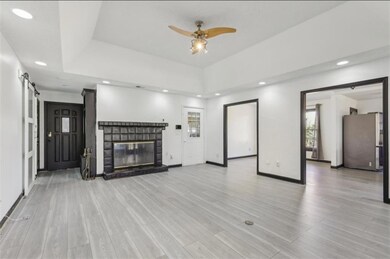 Unfurnished living room featuring a barn door, recessed lighting, a brick fireplace, a tray ceiling, and light wood finished floors