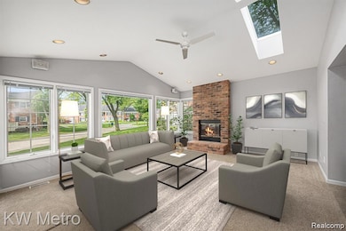 Carpeted living room with vaulted ceiling, a brick fireplace, recessed lighting, a ceiling fan, and a skylight
