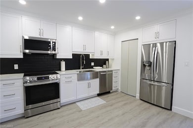 Kitchen with appliances with stainless steel finishes, a sink, white cabinetry, recessed lighting, and ornamental molding