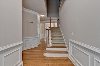 Staircase with wood finished floors, a decorative wall, wainscoting, and ornamental molding