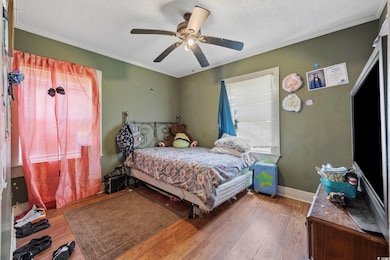 Bedroom featuring a textured ceiling, ornamental molding, wood finished floors, and a ceiling fan