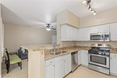 Kitchen with appliances with stainless steel finishes, white cabinetry, light stone countertops, light tile patterned floors, and a peninsula