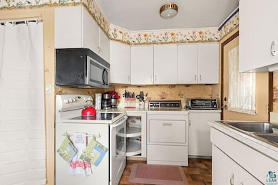 Kitchen featuring white electric range, stainless steel microwave, washer and clothes dryer, light countertops, and white cabinetry