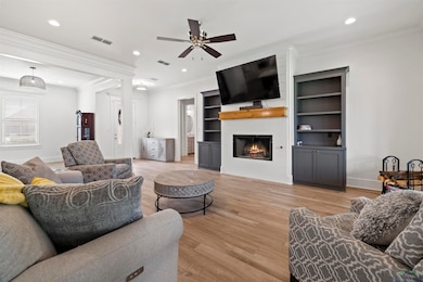 Living room with a ceiling fan, light wood-type flooring, ornamental molding, a large fireplace, and recessed lighting