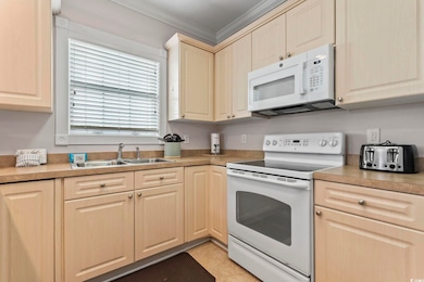 Kitchen with white appliances, light countertops, crown molding, and light tile patterned flooring