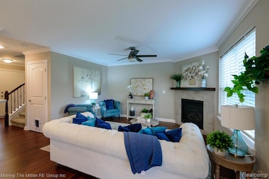 Living room with stairway, crown molding, a fireplace, dark wood-style floors, and a ceiling fan