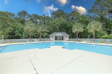 Community pool with fence, view of scattered trees, and a patio