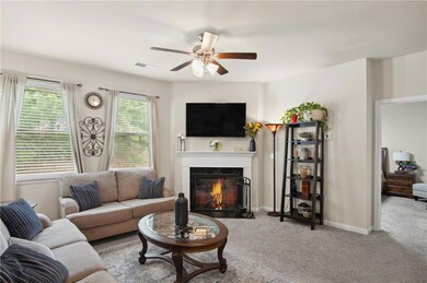 Living area featuring a fireplace with flush hearth, carpet flooring, and a ceiling fan