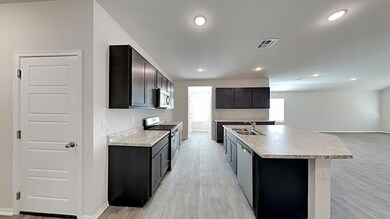 Kitchen featuring stainless steel appliances, light wood-style floors, a kitchen island with sink, recessed lighting, and dark brown cabinetry