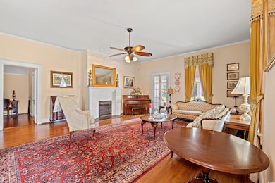 Living room featuring wood finished floors, ceiling fan, ornamental molding, and a fireplace