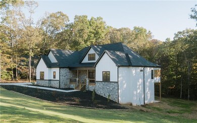 Modern farmhouse style home with a porch, stone siding, a front yard, and board and batten siding