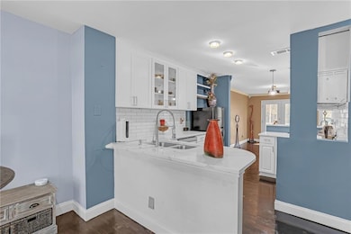 Kitchen with tasteful backsplash, glass insert cabinets, light stone counters, white cabinets, and dark wood finished floors