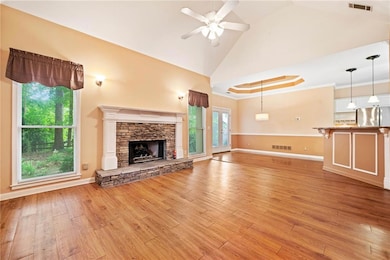 Unfurnished living room with a ceiling fan, light wood-type flooring, vaulted ceiling, baseboards, and a stone fireplace