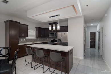 Kitchen with appliances with stainless steel finishes, decorative backsplash, a breakfast bar, light countertops, and a center island