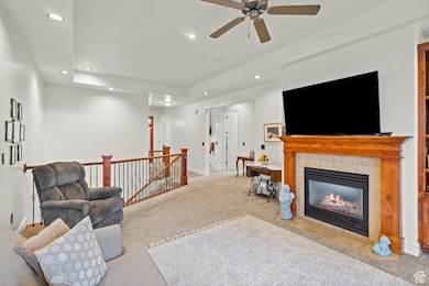 Carpeted living area with recessed lighting, a ceiling fan, a tile fireplace, and a raised ceiling