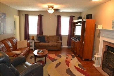 Open concept family room with newer wood flooring, ceiling fan with light and a wood burning fireplace.