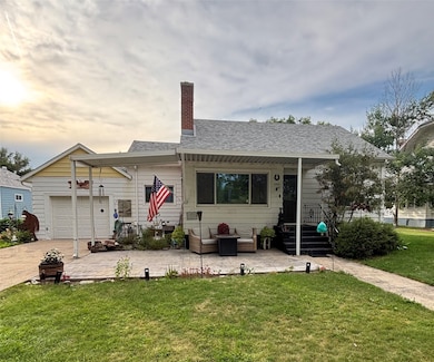 View of front of house with a chimney, a front lawn, a patio, an attached garage, and roof with shingles