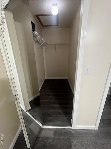 Walk in closet with attic access and dark wood finished floors