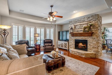 Cozy and inviting living room with a custom stone fireplace and a bay window overlooking the backyard oasis. Plantation shutters throughout.