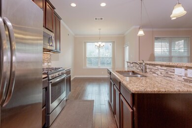 Kitchen featuring tasteful backsplash, stainless steel appliances, hanging light fixtures, light stone countertops, and ornamental molding