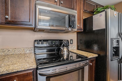 Kitchen featuring appliances with stainless steel finishes, dark brown cabinets, and light stone counters