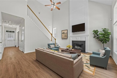 Living room featuring wood finished floors, stairway, a fireplace with flush hearth, ceiling fan, and a towering ceiling