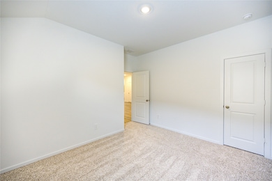 This photo shows a bright, neutral-toned room with clean white walls and beige carpet. The room features a recessed ceiling light and two doors, one slightly open, leading to a hallway with wood flooring. The space feels inviting and versatile, perfect for a bedroom or home office.