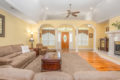 Living room featuring a ceiling fan, decorative columns, wood finished floors, lofted ceiling, and a fireplace