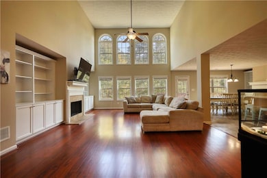 Living room with dark wood finished floors, a high ceiling, a premium fireplace, a chandelier, and a ceiling fan