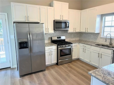 Kitchen with healthy amount of natural light, light stone counters, appliances with stainless steel finishes, and white cabinets