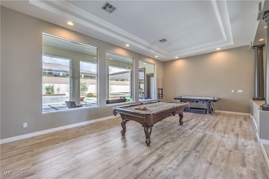 Rec room with a raised ceiling, billiards table, light wood-style flooring, crown molding, and baseboards