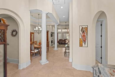 Foyer featuring arched walkways, a chandelier, ornate columns, light tile patterned floors, and crown molding