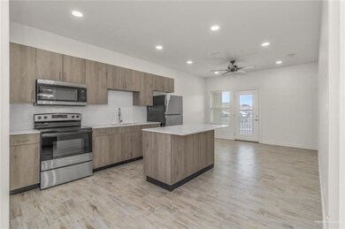 Kitchen with stainless steel appliances, a sink, ceiling fan, light countertops, and a kitchen island