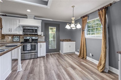 Kitchen with white cabinetry, stainless steel appliances, decorative backsplash, ornamental molding, and decorative light fixtures