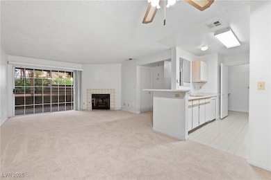 Unfurnished living room with a textured ceiling, light colored carpet, ceiling fan, and a fireplace