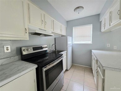 Kitchen with electric stove, under cabinet range hood, light countertops, white cabinetry, and light tile patterned floors